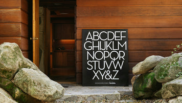 A large black canvas with the alphabet set in Neutraface. It sits outside an Earl Wear House.